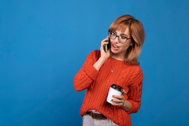 Porträt einer lächelnden jungen lässigen Frau, die auf Handy lokalisiert über blauem Hintergrund spricht.