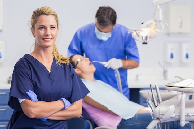 Porträt einer lächelnden Krankenschwester ihre Arme gekreuzt und Zahnarzt mit dem Patienten hinter ihm