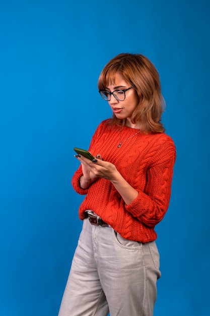 Porträt einer lächelnden lässigen Frau, die Smartphone über blauem Hintergrund hält.