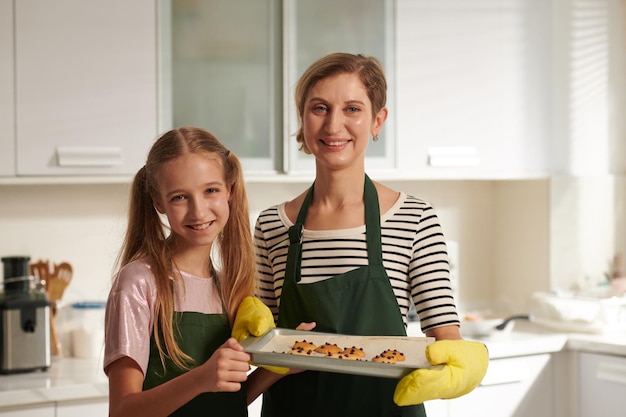 Porträt einer lächelnden Mutter und ihrer Tochter im Teenageralter, die ein Tablett mit gemeinsam gebackenen Keksen halten