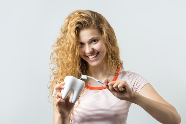Porträt einer lächelnden netten Frau mit dem roten gelockten Haar, das die Zahnbürste lokalisiert auf einem weißen Hintergrund hält