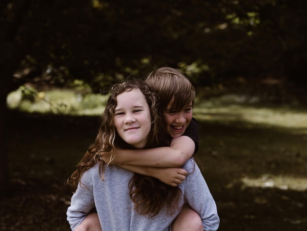 Porträt einer lächelnden Schwester, die ihren Bruder im Wald auf dem Rücken trägt