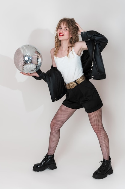 Foto porträt einer lächelnden tänzerin, die einen disco-ball in der hand hält und in die kamera schaut.