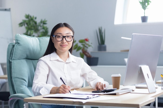 Porträt einer lächelnden und schauenden jungen, schönen und erfolgreichen asiatischen Geschäftsfrau