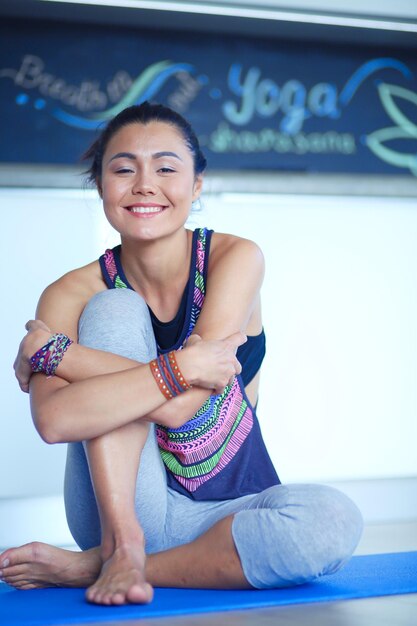 Porträt einer lächelnden Yoga-Frau, die nach dem Training im Yoga-Studio auf einer Yoga-Matte sitzt Yoga-Frau