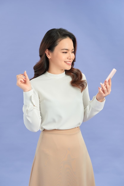 Porträt einer lächelnden zufälligen Frau, die Smartphone über lila Hintergrund hält