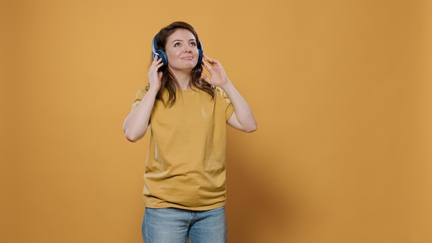 Porträt einer lässigen Frau mit drahtlosen Kopfhörern, die fröhliche Musik hört und allein im Studio tanzt. Selbstbewusster junger Mensch, der zum ersten Mal eine Band entdeckt und Partyhits genießt.