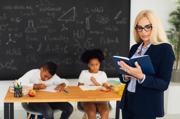 Porträt einer Lehrerin, die auf dem Hintergrund eines Klassenzimmers und von Schulkindern steht