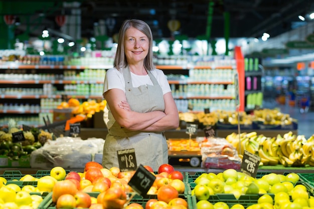 Porträt einer leitenden Managerin eines Lebensmittelgeschäfts-Supermarkts, die in Arbeitskleidung steht und mit verschränkten Armen lächelnd in die Kamera schaut