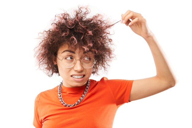 Porträt einer lockigen jungen Frau, die Haare berührt, mit unzufriedenem Gesicht, isoliert auf weißem Studiohintergrund, Konzept für beschädigtes Haar