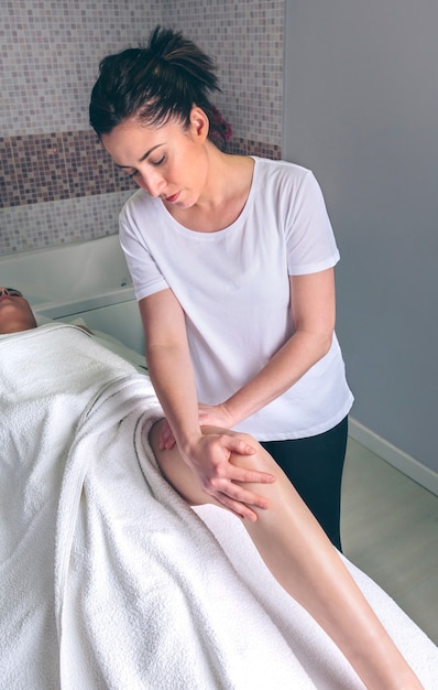 Porträt einer Massagetherapeutin, die Lymphdrainagemassage an den Beinen einer jungen Frau in einem klinischen Zentrum macht. Medizin-, Gesundheits- und Schönheitskonzept.