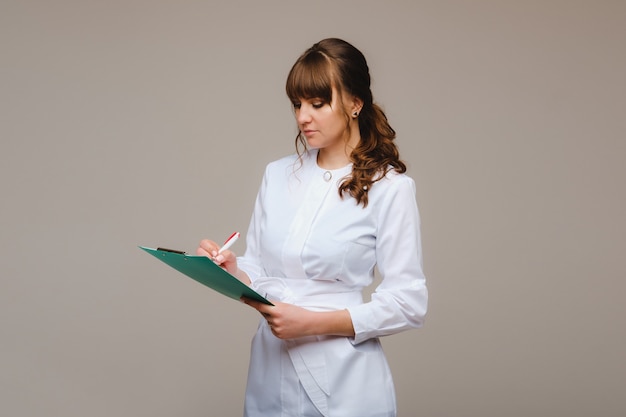 Porträt einer medizinischen Arbeiterin in einem grauen Hintergrund mit einem medizinischen Bericht. Ärztin mit einem Notizblock