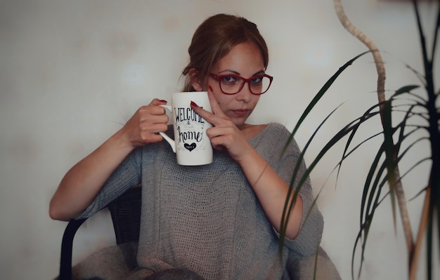 Porträt einer mittleren erwachsenen Frau, die zu Hause sitzt und einen Becher hält