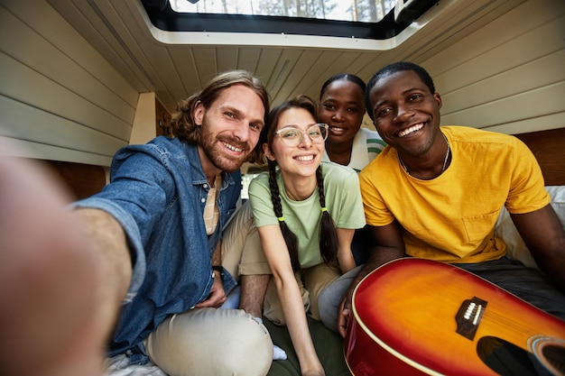 Porträt einer multiethnischen Gruppe von Freunden, die in die Kamera lächeln, während sie Gitarre spielen und lustige t