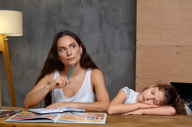 Porträt einer Mutter, die ihrer kleinen süßen und süßen Tochter hilft, ihre Hausaufgaben im Haus zu machen. Glückliche Familie.