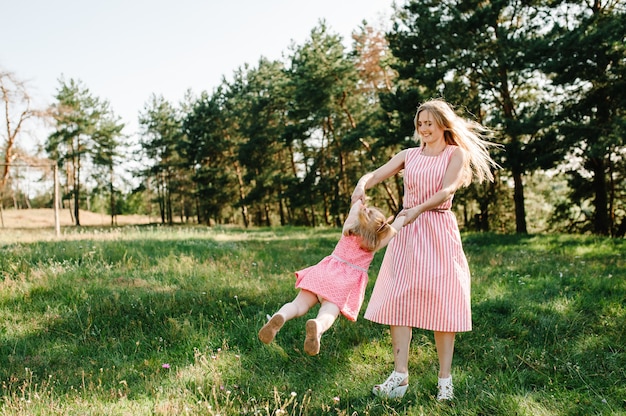 Porträt einer Mutter hält, wirft und dreht die Tochter an den Händen in der Natur im Sommerurlaub. Mutter und Mädchen, die bei Sonnenuntergang im Park spielen. Konzept der freundlichen Familie. Nahaufnahme.