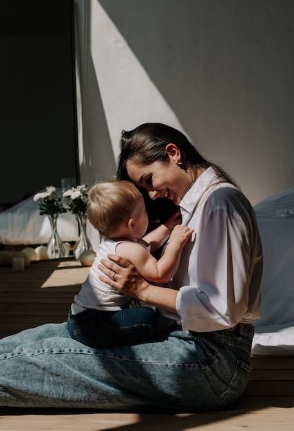 Porträt einer Mutter mit einer kleinen Tochter, die sich in einem Raum im Sonnenlicht umarmt