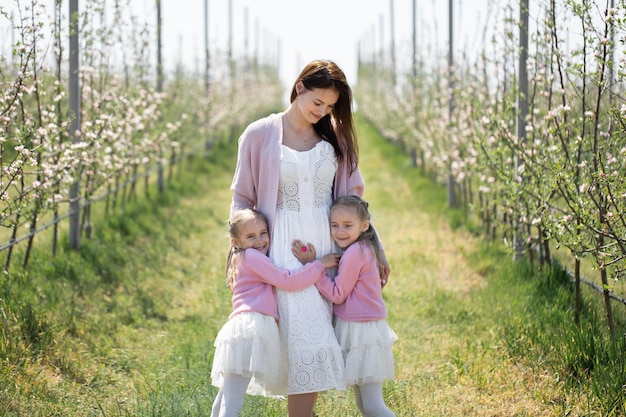 Porträt einer Mutter und ihrer Zwillingstöchter in einem blühenden Apfelgarten