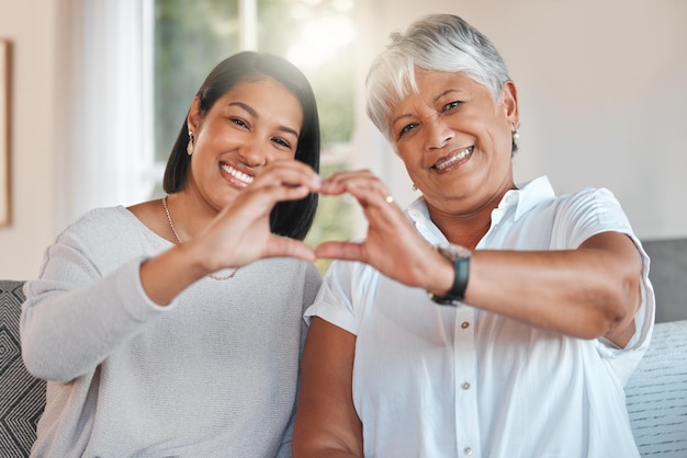 Porträt einer Mutter und Tochter, die ihre Hände zusammenhalten, um eine Herzform auf dem Sofa zu bilden