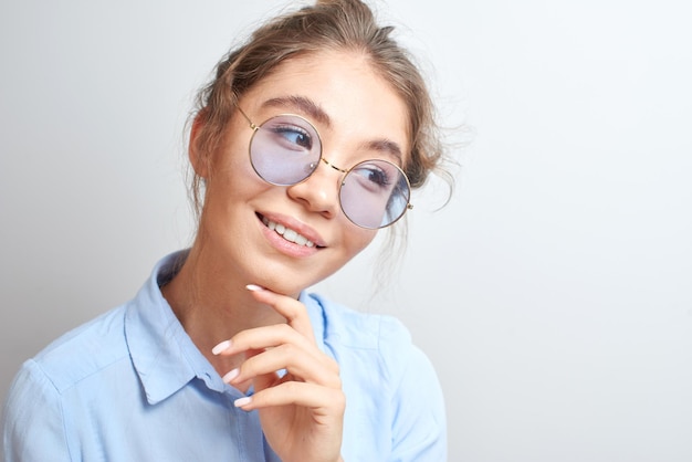 Porträt einer nachdenklichen asiatischen kasachischen jungen Frau mit Haarknoten auf dem Kopf in stylischer Brille, die ein Hemd im weißen Studio trägt, denkendes Mädchen