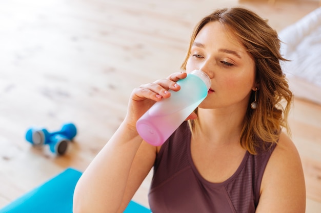 Porträt einer netten jungen Frau, die Wasser nach einem Yoga-Training trinkt