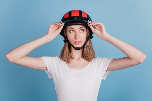 Foto porträt einer neugierigen, verträumten dame, die einen motorradhelm trägt, sieht auf blauem hintergrund leer aus