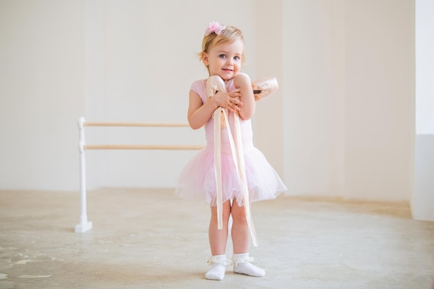 Porträt einer niedlichen blauäugigen Babyballerina in rosa umarmenden Spitzenschuhen