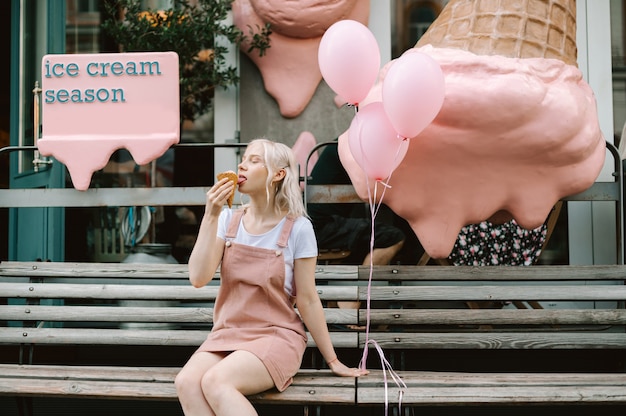 Porträt einer niedlichen Dame, die die Straße mit Eis und Luftballons entlang geht