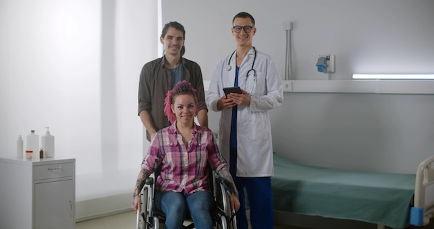 Porträt einer Patientin im Rollstuhl, Ehemann und Arzt, die auf der Krankenstation in die Kamera lächeln