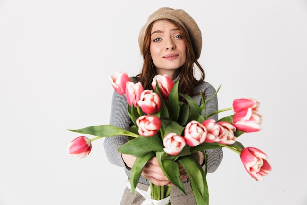 Porträt einer positiven Frau 30er Jahre mit Hut, die einen schönen Blumenstrauß isoliert auf weiß hält