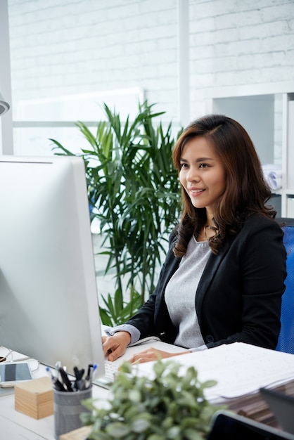 Porträt einer positiven, schönen Geschäftsfrau, die die Arbeit am Computer an ihrem Schreibtisch mit pl...