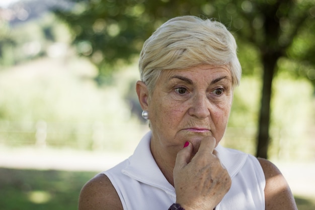 Porträt einer reifen Frau, die mit der Hand am Kinn im Park nachdenklich aussieht