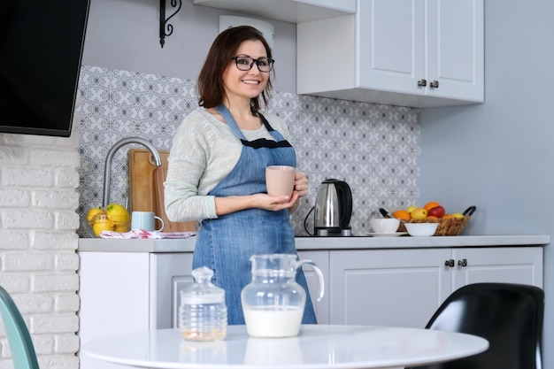 Porträt einer reifen Hausfrau in einer Schürze zu Hause in der Küche mit einer Tasse Tee