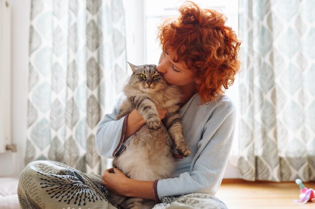 Porträt einer rothaarigen, lockigen jungen Frau mit ihrer geliebten flauschigen Hauskatze