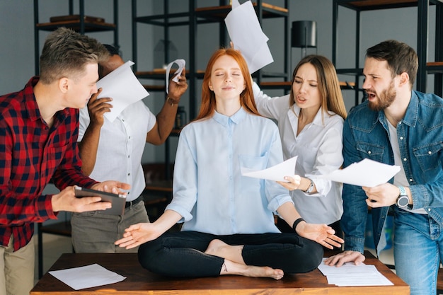 Porträt einer ruhigen jungen Geschäftsfrau, die bei Geschäftstreffen meditiert und Druck vermeidet, der wütende Kollegen nervt Meditative Geschäftsfrau-Yoga-Übungen zum Stressabbau Mitarbeiter schütteln Dokumente