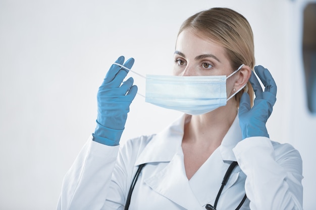 Porträt einer Ärztin in einem weißen Kittel, die vor der Arbeit eine medizinische Maske aufsetzt