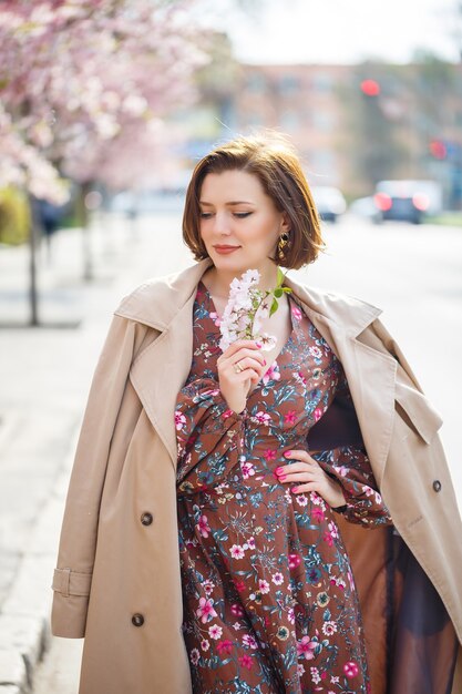 Porträt einer sanften Frau vor dem Hintergrund von Sakura-Blumen. Spazieren Sie durch den blühenden Sakura-Garten. Junge stilvolle Frau, die im Sakura-Park steht und Schönheit genießt