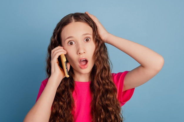 Foto porträt einer schockierten, sprachlosen kleinen dame, die das handy mit offenem mund hält, ruft auf blauem hintergrund an