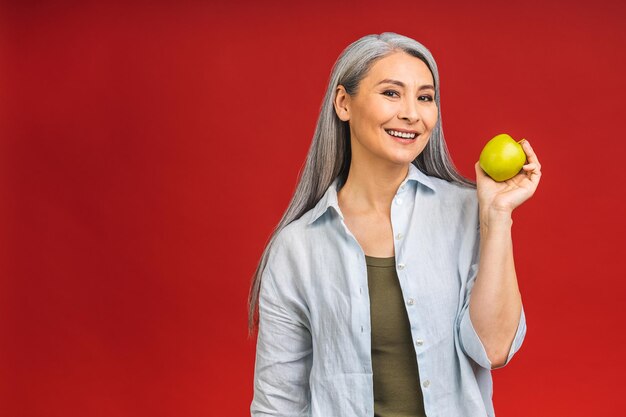 Porträt einer schönen älteren reifen Senior asiatischen Frau im Alter von einem Apfel lächelnd isoliert über rotem Hintergrund Ein Apfel am Tag hält einen Arzt fern