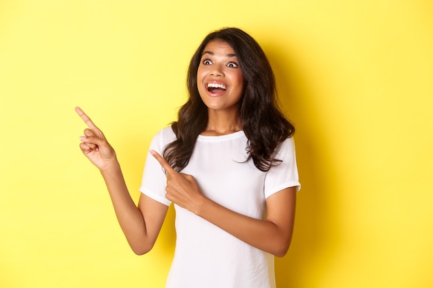 Porträt einer schönen afroamerikanischen Frau, die mit den Fingern zeigt und in die obere linke Ecke schaut und ein tolles Promo-Angebot zeigt, das auf gelbem Hintergrund steht.