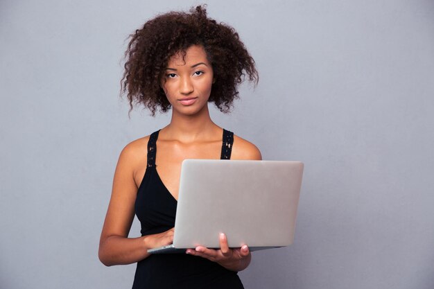 Porträt einer schönen afroamerikanischen Frau unter Verwendung des Laptops über grauer Wand. Blick nach vorne