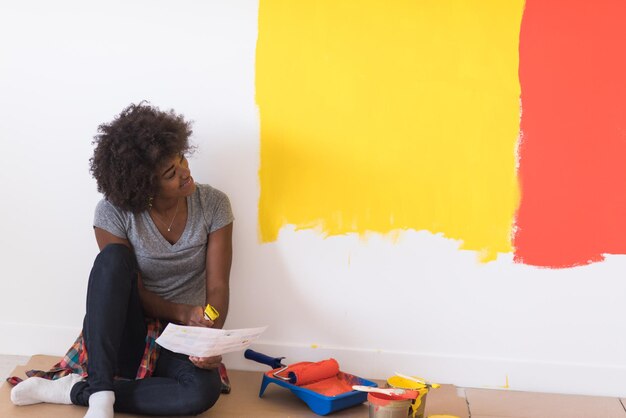 Porträt einer schönen afroamerikanischen Malerin, die nach dem Malen auf dem Boden in der Nähe der Wand sitzt.