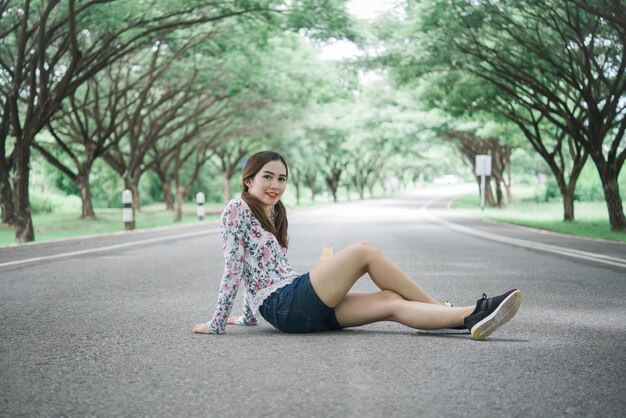 Porträt einer schönen asiatischen Frau, die auf der Straße unter Tunnelbäumen sitzt