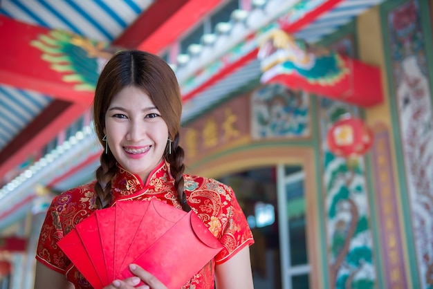 Porträt einer schönen asiatischen Frau in Cheongsam-Kleid mit rotem Umschlag in der HandThailänderFrohes chinesisches Neujahrskonzept