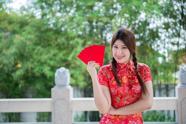 Porträt einer schönen asiatischen Frau in Cheongsam-Kleid mit rotem Umschlag in der HandThailänderFrohes chinesisches Neujahrskonzept