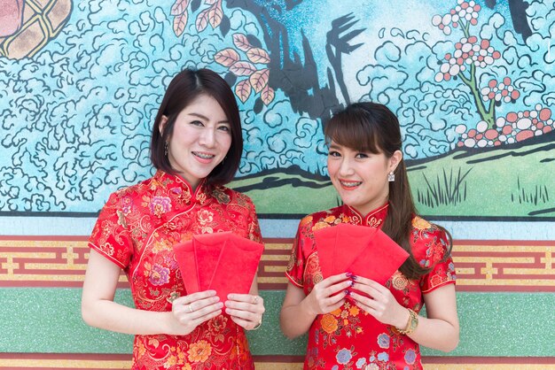 Porträt einer schönen asiatischen Frau in Cheongsam-Kleid mit rotem Umschlag in der HandThailänderFrohes chinesisches Neujahrskonzept