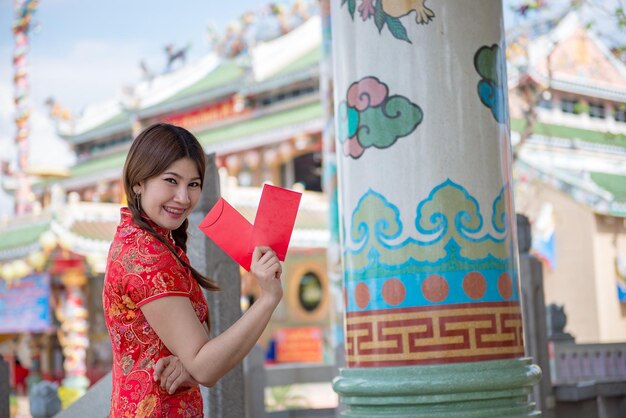 Porträt einer schönen asiatischen Frau in Cheongsam-Kleid mit rotem Umschlag in der HandThailänderFrohes chinesisches Neujahrskonzept