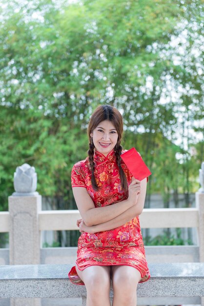 Porträt einer schönen asiatischen Frau in Cheongsam-Kleid mit rotem Umschlag in der HandThailänderFrohes chinesisches Neujahrskonzept