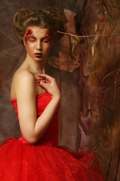 Porträt einer schönen blonden Frau im roten Kleid. Kreatives Make-up und Frisur. In einem Fantasiehaus gedreht.