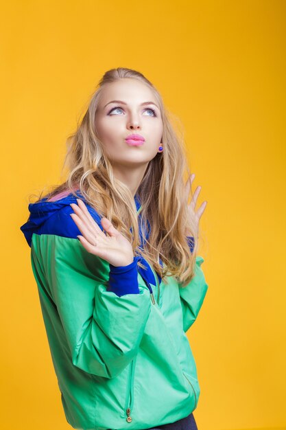 Porträt einer schönen blonden Frau in lässiger bunter leuchtend grüner Sommerkleidung auf gelbem Hintergrund